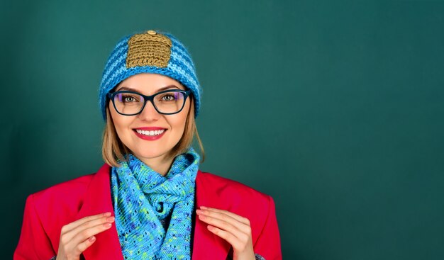 Foto moda autunno/inverno. moda donna che indossa giacca rossa, cappello, sciarpa in occhiali neri. ragazza sorridente con gli occhiali con trucco, labbra rosse brillanti, indossa cappotto rosso, cappello blu e sciarpa. copia spazio per pubblicizzare