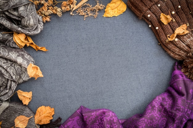 Autumn winter flat lay. Brown knitted beanie, purple scarf and dry leaves on blue