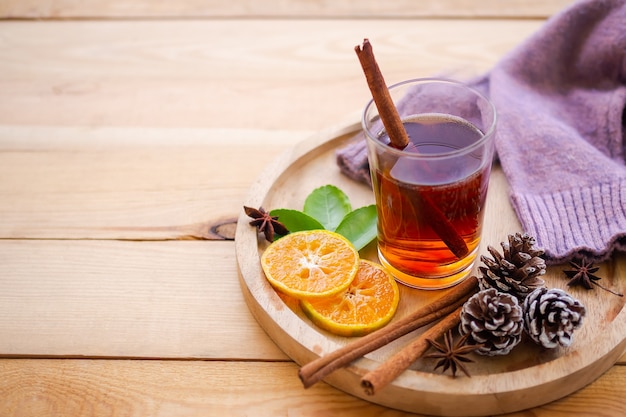 Autumn, winter hot tea drink concept. tea in glass with spices and star anise spice fruits, flaky orange, pine cones, sweater on wooden plate with wood background.