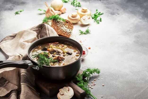 Autumn or winter meat vegetable mushroom hot soup with beef and wholegrain barley With black breav and parsley top view gray kitchen table copy space