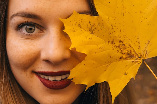 Autumn woman holding yellow maple leaves and hiding her eye