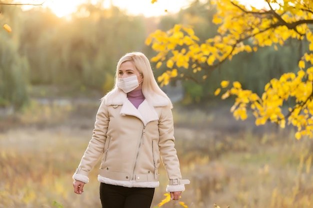 Autumn woman in medical protective face mask walking outdoors, fall season portrait