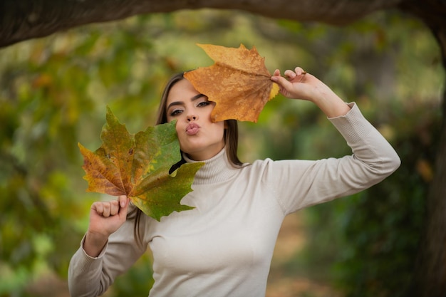 秋の黄色のカエデの葉を持つ秋の女性の屋外ポートレート秋の紅葉を持つ美しいモデルはあなたがたに落ちる