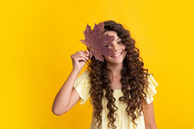 Autumnal mood Child girl in autumn leaves Teenager girl with oak and maple leaf isoalted on yellow background Happy teenager positive and smiling emotions of teen girl