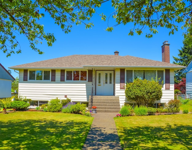 Average family house with green lawn and trees in front on blue sky background