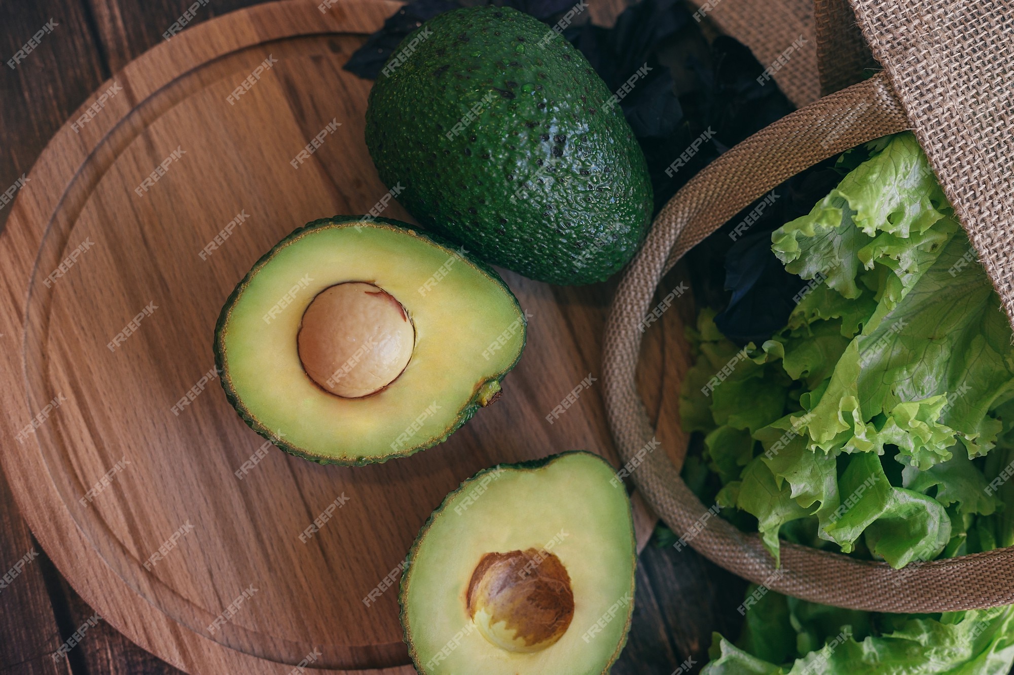 Premium Photo  Avocado cut in half on a wooden table, coriander and basil  next to a straw bag. concept of proper and healthy nutrition, vegetarianism.