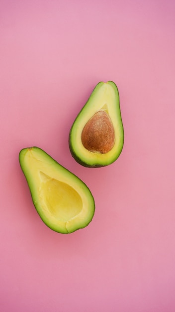 avocado cut in halves on pink surface