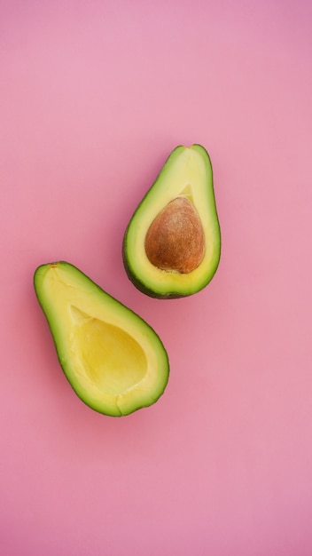 Avocado tagliato a metà sulla superficie rosa