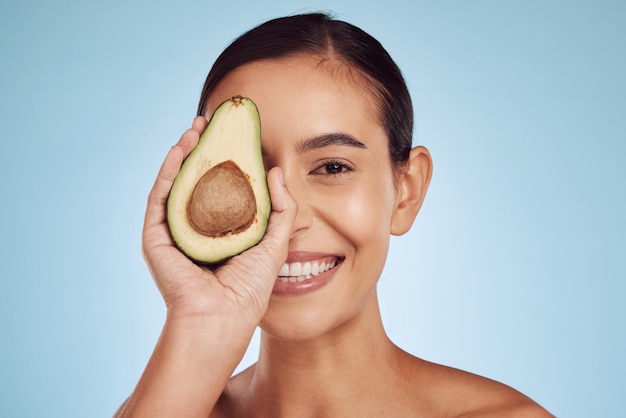 Avocado eye skincare and woman in portrait for healthy face or natural cosmetics on studio blue background Happy person or model of green fruits vitamin d benefits and dermatology or beauty health