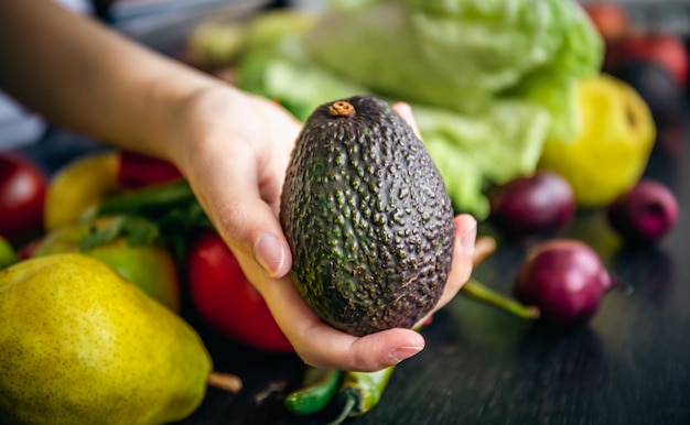 Avocado in una mano femminile su uno sfondo sfocato con verdure