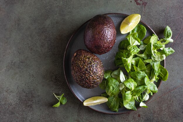 Avocado, groene bladerensalade en kalkplakken op groene concrete achtergrond. Gezonde vetten. Bovenaanzicht.