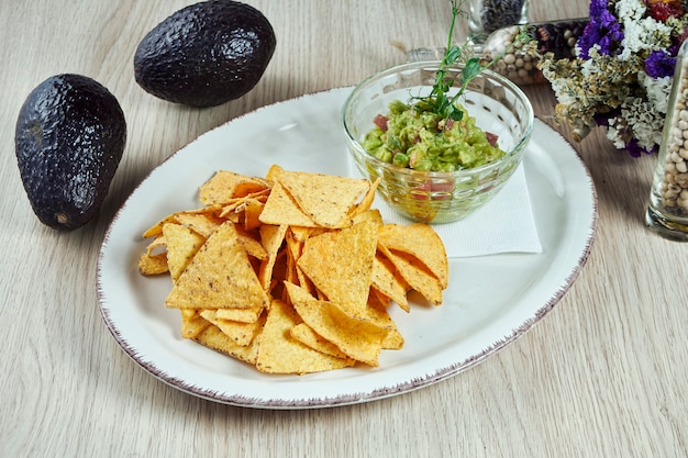 Avocado guacamole met nacho chips op een lichte plaat op een houten tafel. close-up op populaire mexicaanse snack