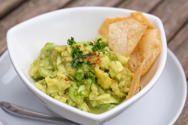 Avocado guacamole with tortilla chips in a white bowl Green guacamole and dipping tortilla chips