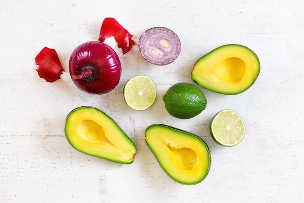 Avocado halves, limes and onions - basic guacamole ingredients on white working board, flat lay photo