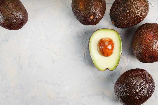 Avocado halves with whole Hass fruits on a surface of gray concrete