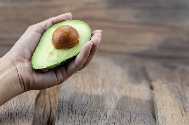 Avocado in mano con uno sfondo in legno.