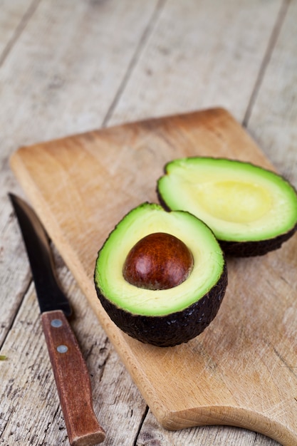 Avocado and knife on cutting board on old wooden table 