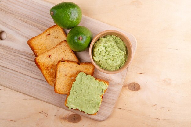 Foto la poltiglia di avocado giaceva su fette di pane tostato su una tavola da taglio di legno posta su un tavolo di legno