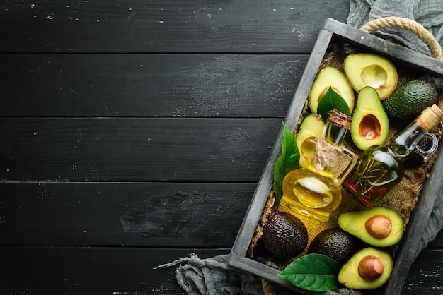 Avocado oil and fresh avocados on a black background Rustic style Top view Free space for your text