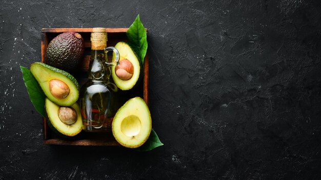 Avocado oil and fresh avocados on a black background Rustic style Top view Free space for your text