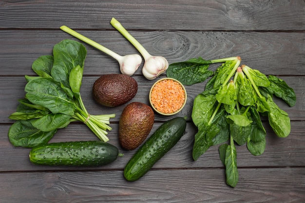 Foto avocado, lenticchie rosse e aglio. foglie di spinaci e cetrioli sul tavolo. fondo in legno scuro. disposizione piatta.