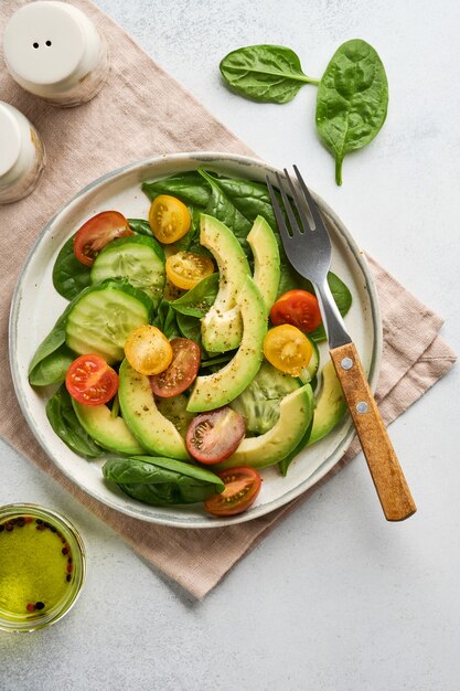 Insalata fresca di avocado, rosso, giallo, amarena, spinaci e cetriolo con spezie pepe e olio d'oliva in una ciotola grigia su sfondo grigio ardesia, pietra o cemento. concetto di cibo sano. vista dall'alto.