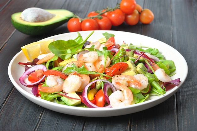 Avocado salad with shrimps, cherry tomatoes, red onion and green leaves