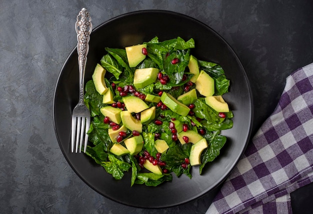 avocado salad with spinach and pomegranate in a black plate on black background.