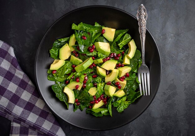 avocado salad with spinach and pomegranate in a black plate on black background