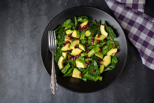 Avocado salad with spinach and pomegranate in a black plate on black background