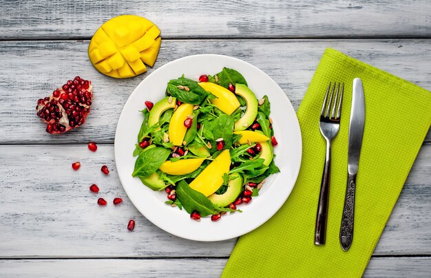 Avocado salad with spinach and pomegranate on a white plate on a wooden table