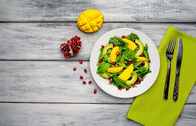 Avocado salad with spinach and pomegranate on a white plate on a wooden table