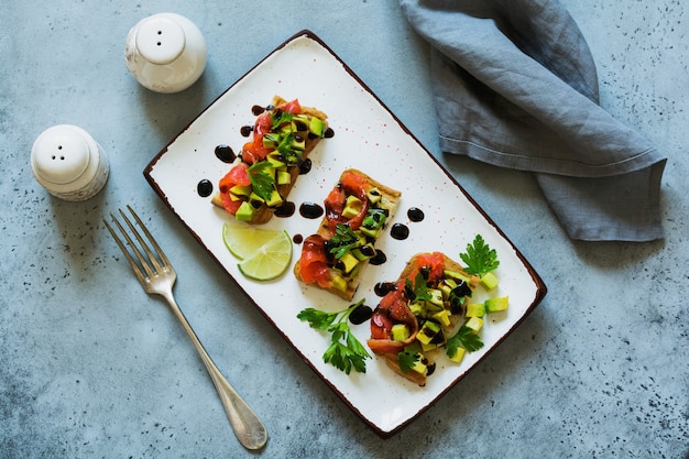 Avocado and salmon sandwiches with balsamic sauce and cilantro on old olive board. Top view.