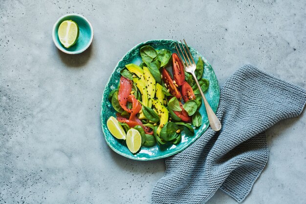 Avocado, salmon, spinach, tomato, pine nuts and black sesame salad in gray ceramic plate. Top view.