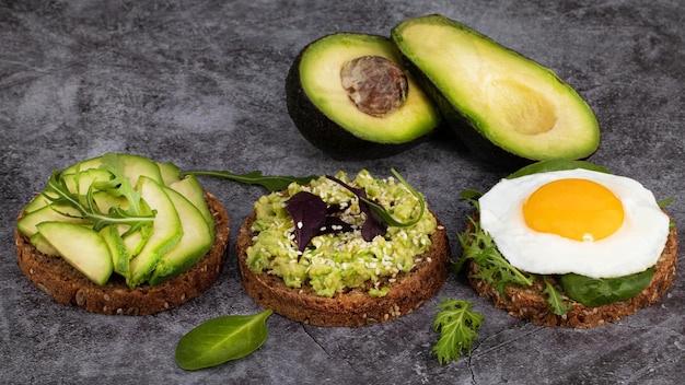 Avocado sandwich on dark rye bread with spinach and fried egg on a dark background.