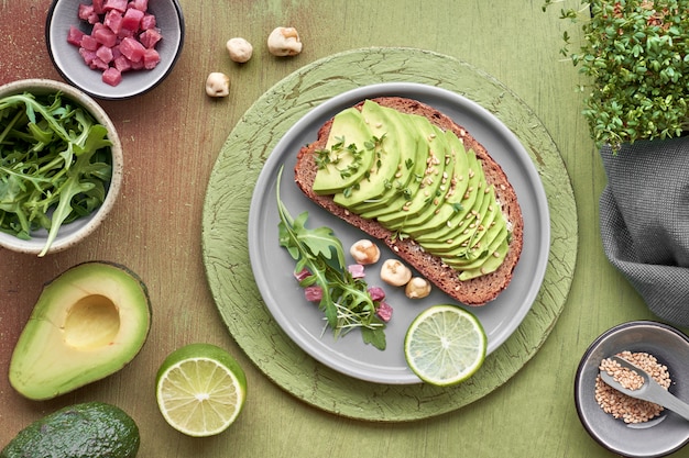 Avocado sandwich and green salad with ham cubes on brown-green textured background