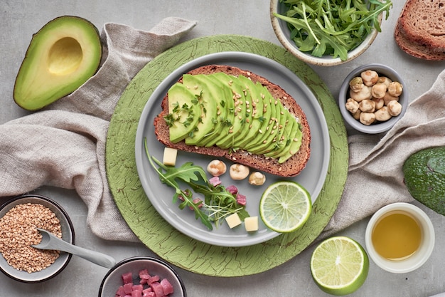 Avocado sandwich and green salad with ham cubes on brown-green textured 