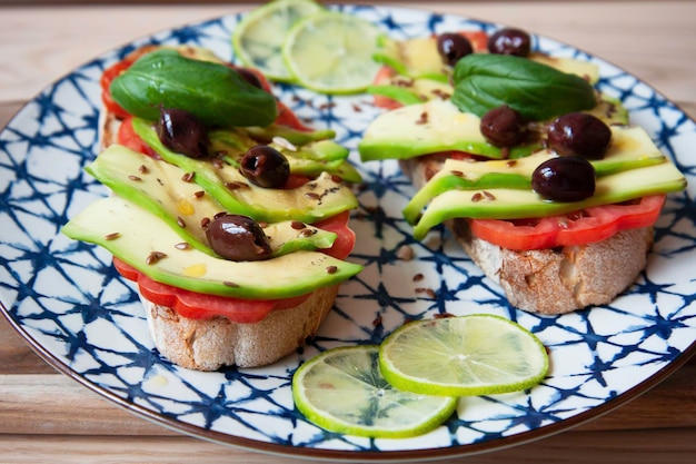 Avocado sandwich toast on ceramic vintage dish Fresh vegetarian ingredients used on brunch meal Bruschetta Avocado Tomatoes Olives Flaxseed Basil Lime Healthy lifestyle Raw food concept