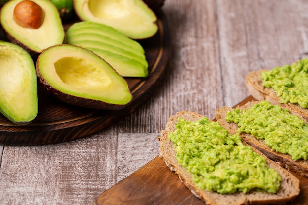 Avocado sandwiches next to cutted ones on wooden board.