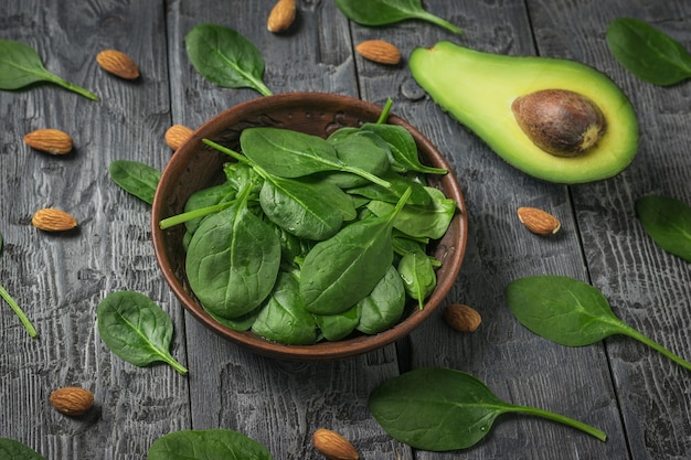 Avocado, spinach leaves and almonds on a wooden table.\
ingredients for the drink and salad.