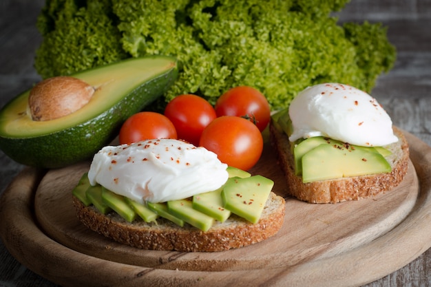 Pane tostato con avocado, pomodorini e uova in camicia su legno. colazione con cibi vegetariani, dieta sana.