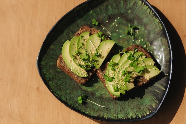 Avocado toast on green plate Vegetarian food concept Fresh food at home Sandwich with avocado and rye bread sesame seeds and mustard seedings Top view
