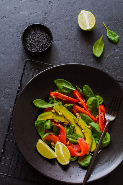 Avocado, zalm, spinazie, tomaat, pijnboompitten en zwarte sesamsalade in een zwarte keramische plaat. Bovenaanzicht.