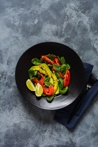 Avocado, zalm, spinazie, tomaat, pijnboompitten en zwarte sesamsalade in een zwarte keramische plaat. Bovenaanzicht.