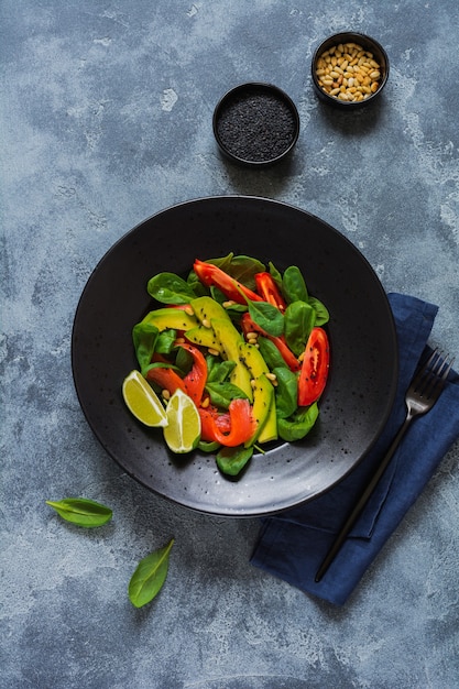 Avocado, zalm, spinazie, tomaat, pijnboompitten en zwarte sesamsalade in een zwarte keramische plaat. Bovenaanzicht.