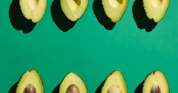 Avocados from above lined up on green background with hard light