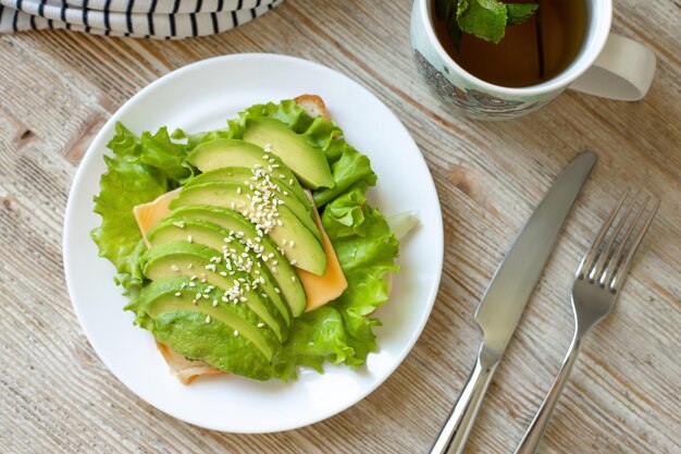 Avocadotoast op tarwebrood met kaassalade en sesamzaadjes op een witte plaat op een houten tafel