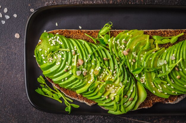 Avocadotoost met roggebrood en zaden op zwarte plaat, donkere achtergrond, hoogste mening.