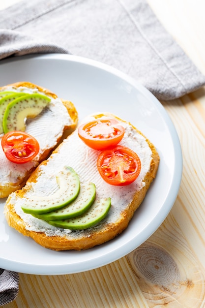 Avocadotoosts met roomkaas op een witte plaat. Toast met avocado en cherrytomaatjes op een linnen servet. Gezond eten. Detailopname