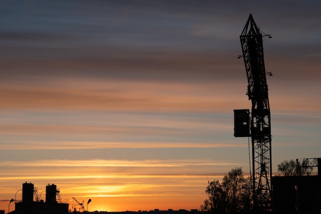 Avond schets van de stad Het silhouet van de fabriek tegen de lucht of zonsondergang De torenkraan werkt op het grondgebied van de fabriek